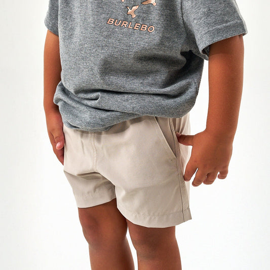 Child wearing a gray t-shirt with a brand logo and beige shorts on a white background