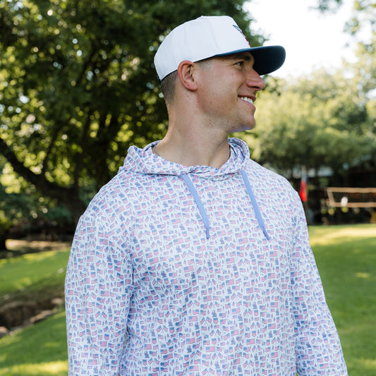 Man wearing a patterned hoodie and cap outdoors with trees in the background