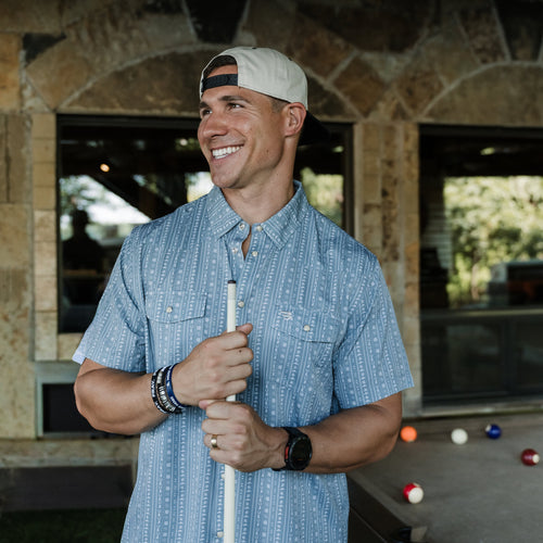 Man holding a pool cue outdoors with a stone building and pool table in the background
