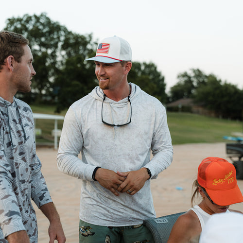 Two men and a child standing outdoors, with one man wearing a cap with an American flag design.