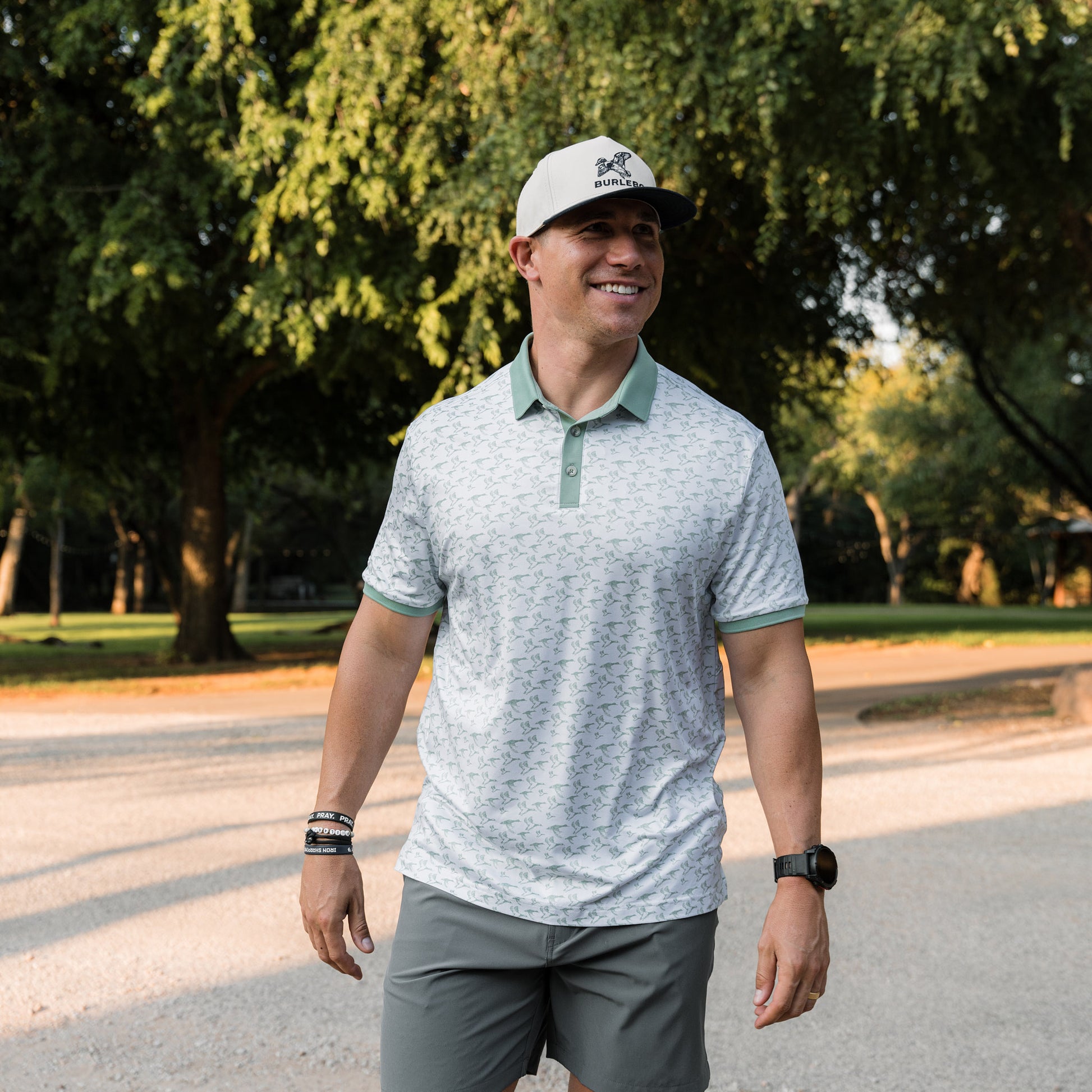 Man wearing a light gray polo shirt with green accents and a cap, standing outdoors.