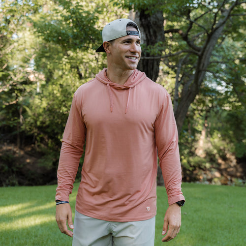 Man wearing a pink long-sleeve shirt and cap outdoors with greenery in the background