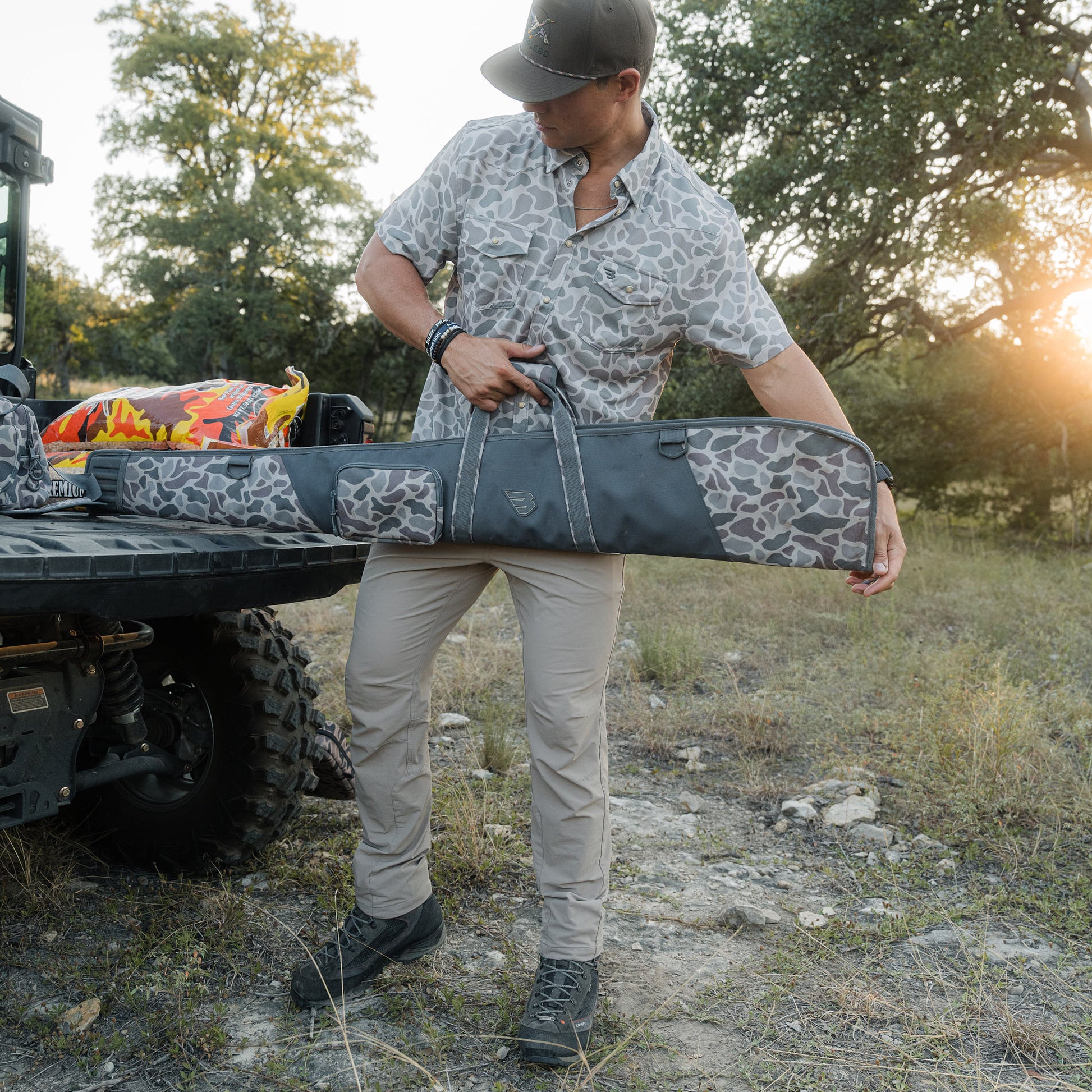 Man holding a patterned rifle case in a natural outdoor setting