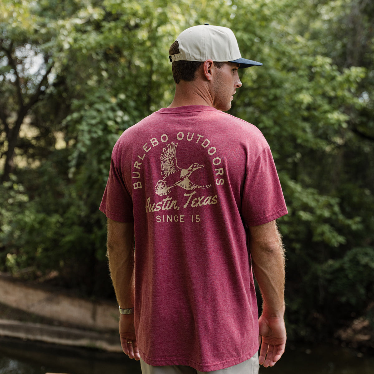 Man wearing a maroon 'Burlebo Outdoors' t-shirt with a logo, standing outdoors.