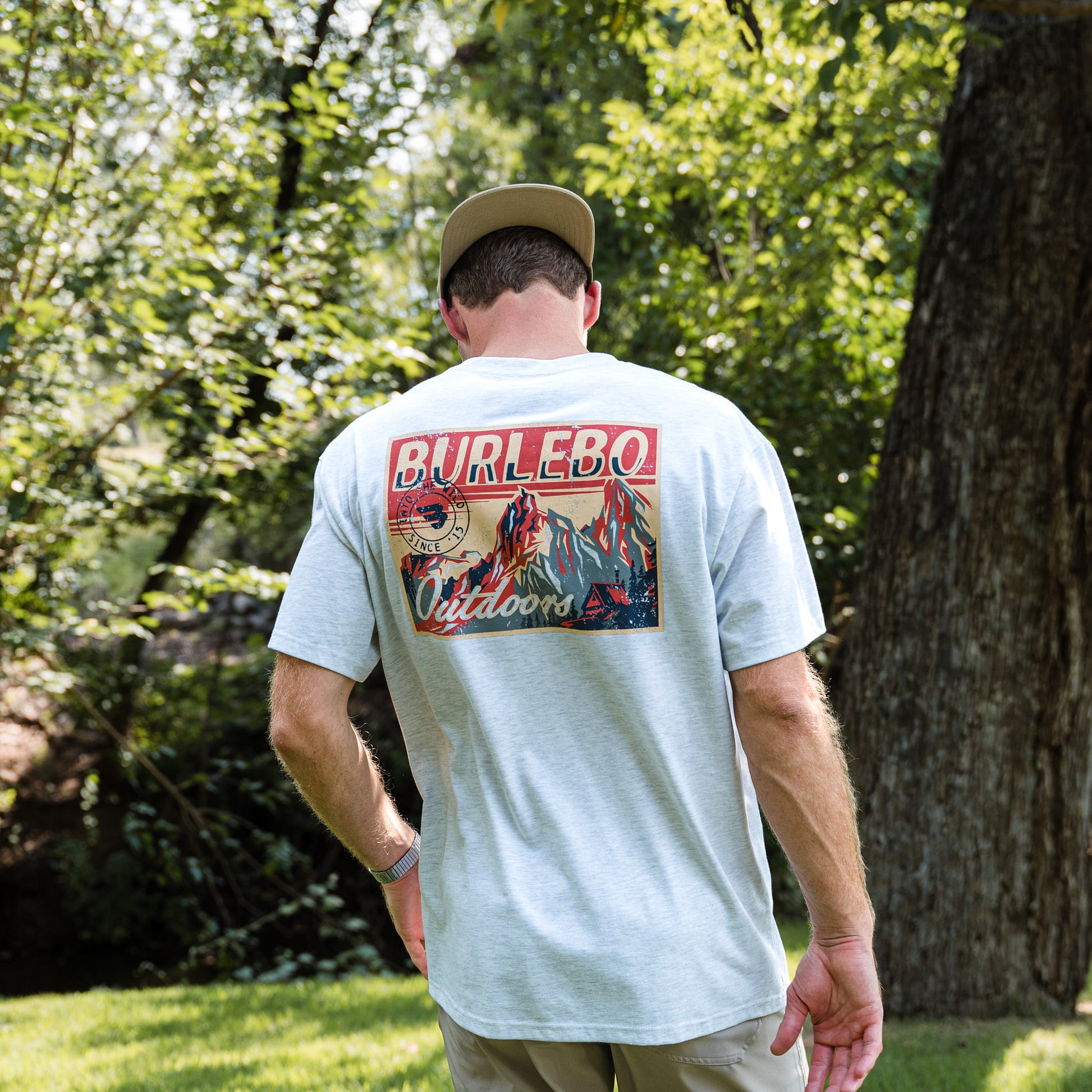 Man wearing a light gray t-shirt with 'Burlebo Outdoors' design outdoors.