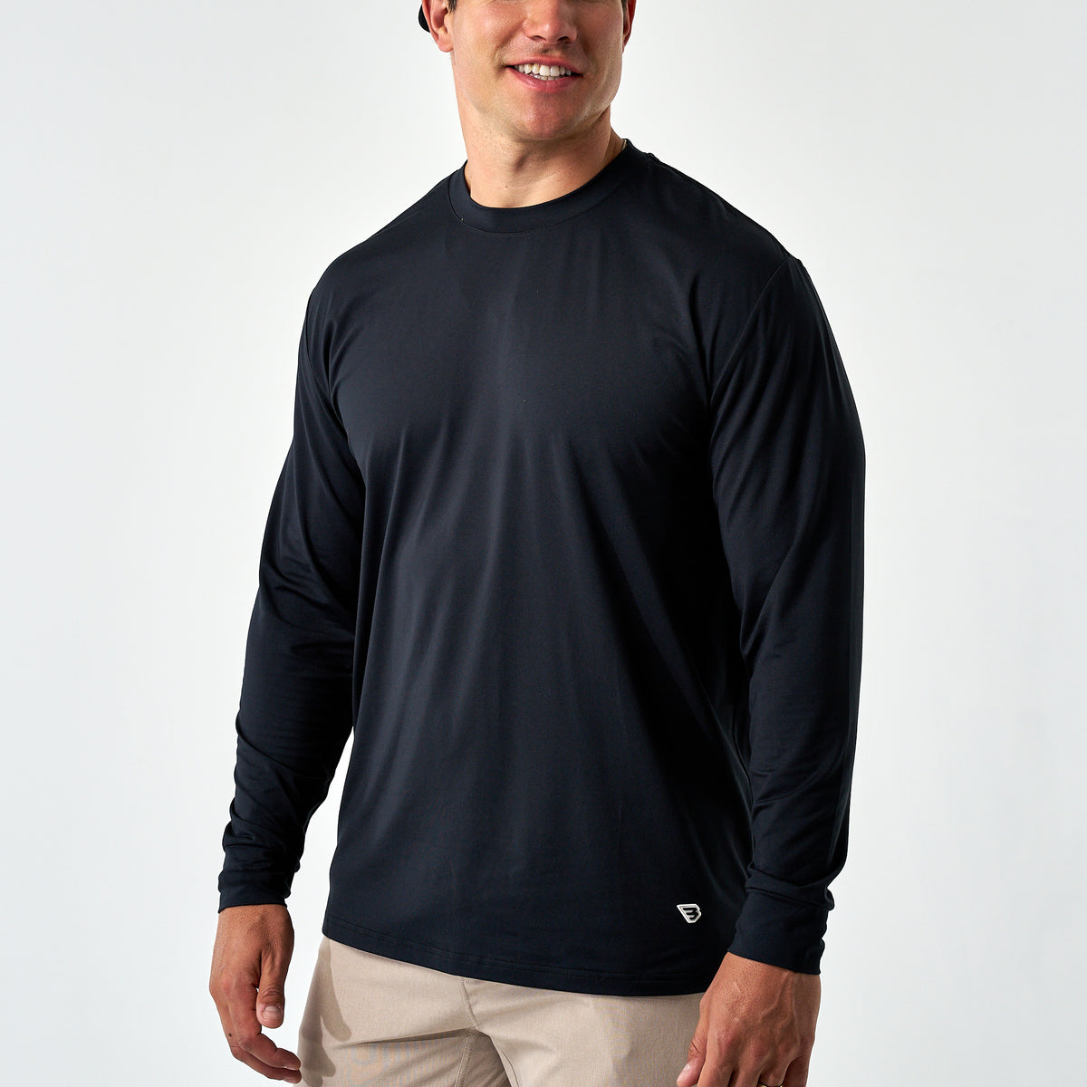 Smiling man wearing the Black Long Sleeve Go To Tee with khaki pants, front view on a white background