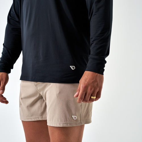 Close-up of the Black Long Sleeve Go To Tee hem with a small white B logo, worn with khaki shorts
