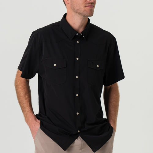 Man wearing a black short-sleeve shirt with button details on a plain background