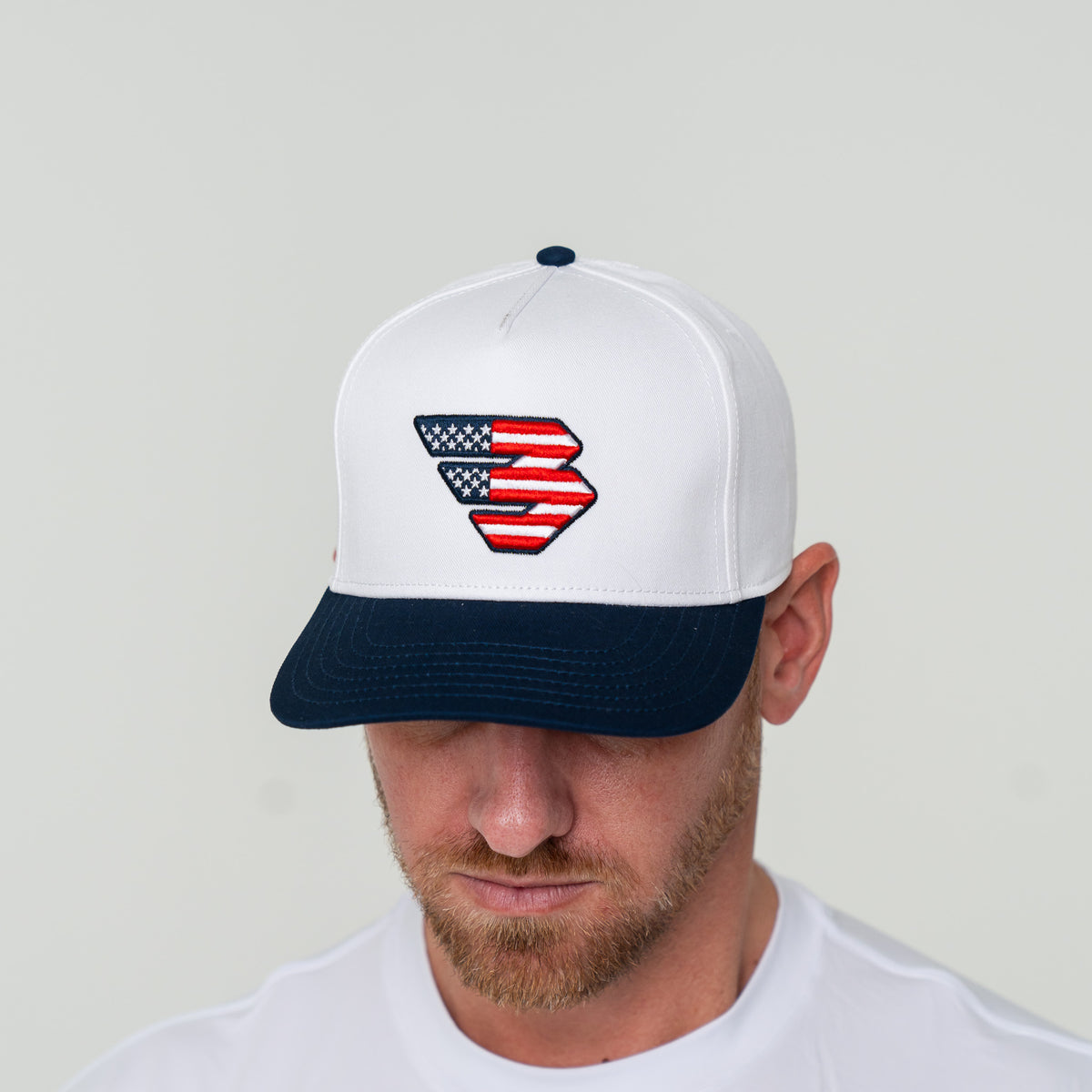 Man wearing the Patriotic Flying B Logo Cap with head tilted down, close-up of the embroidered logo