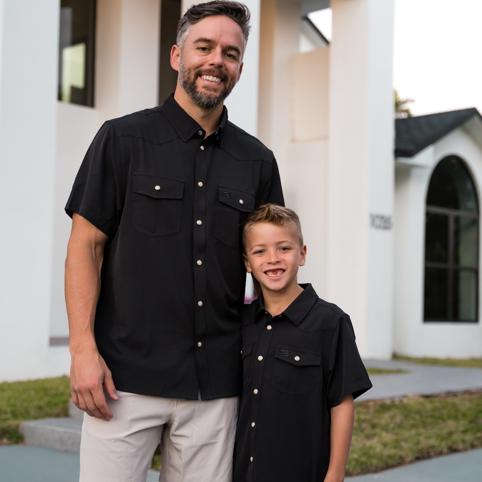 Man and young boy wearing matching black shirts standing in front of a building.