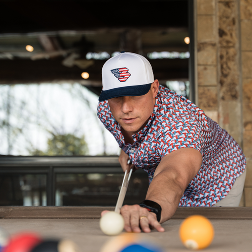 Man leaning over a pool table to take a shot, wearing the Patriotic Flying B Logo Cap