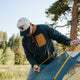 Man in the Dark Olive Micro Fleece and a BURLEBO cap setting up a tent among pine trees