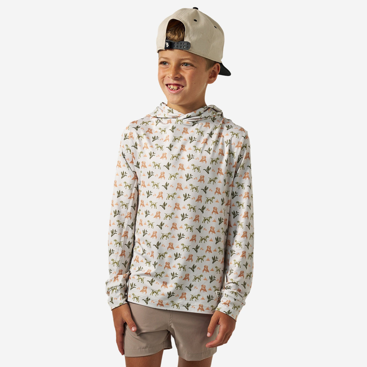 Boy wearing the Mallard Duck Dog Youth Performance Hoodie, cream with a dog and duck print, front view