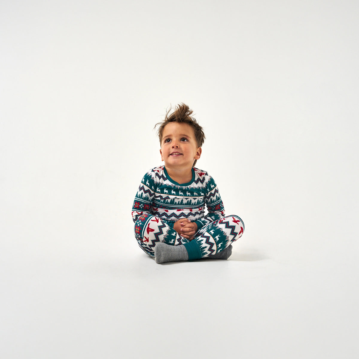 Toddler sitting on the floor in the BURLEBO Outdoors Christmas Youth Pajama Set, looking up